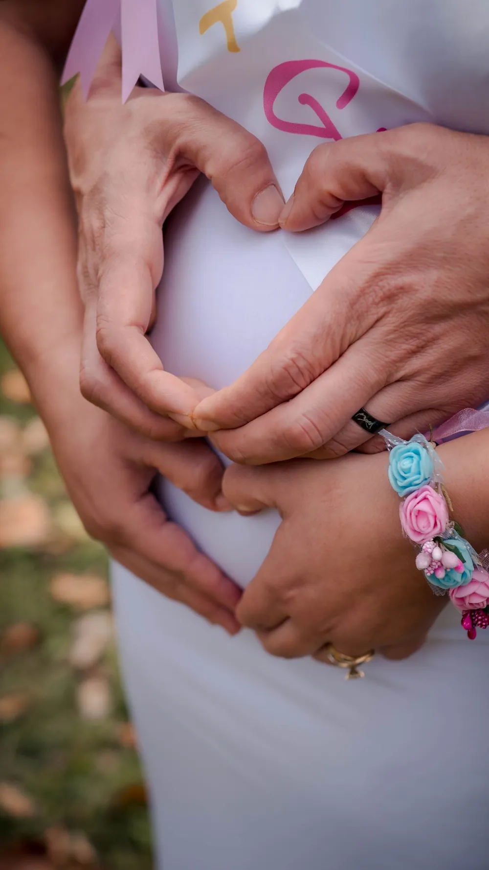Couple's hands forming a heart over a baby bump, with a flower bracelet