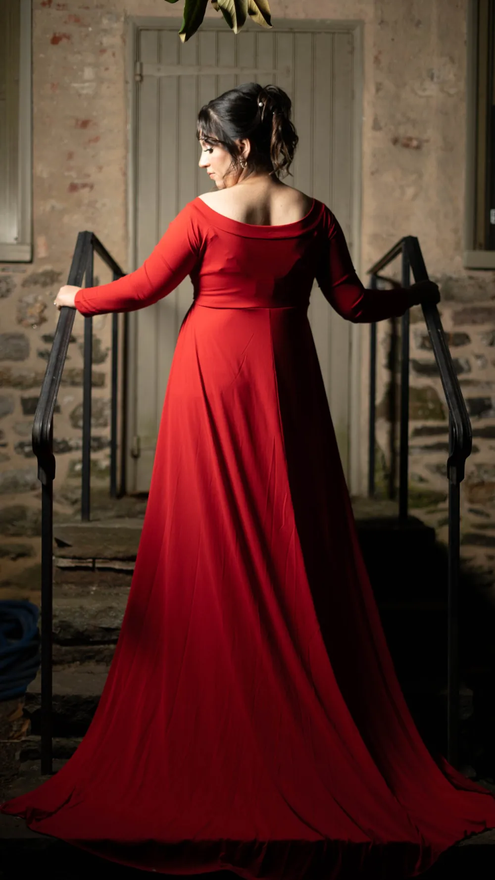 Expecting mother in a red gown on stone steps, seen from behind